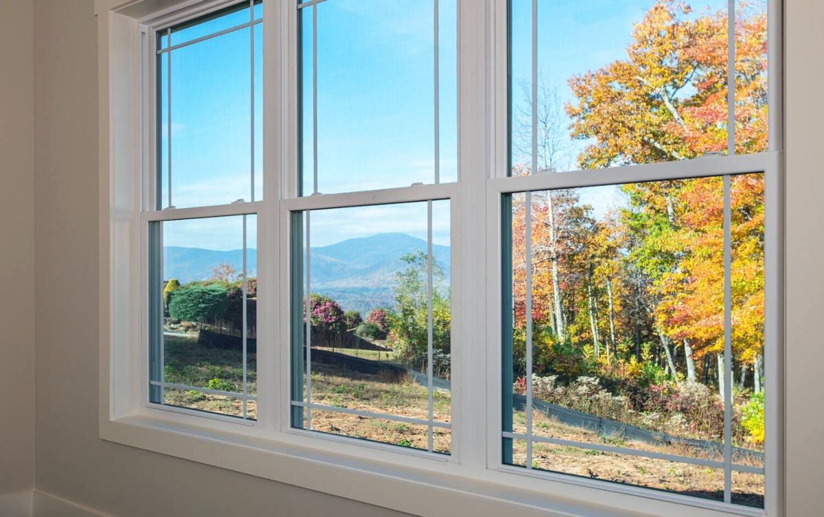 A 3-pane wide window in a bedroom overlooks the mountains in NC with their fall foilage showing.