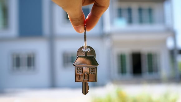 A key with a home trinket on it is held in front of a big home