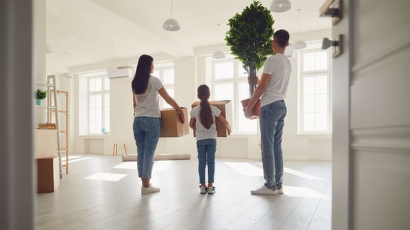 A family of 3 holds boxes while looking around their new home.