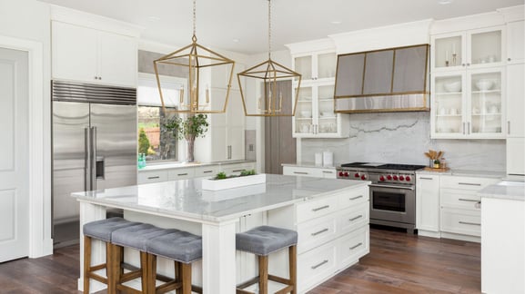 A clean white kitchen has beautiful geometric hanging lights above the island countertop.