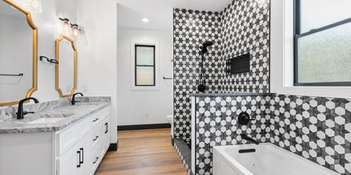 A custom bathroom in a home complete with gold-framed mirrors and an intricate black and white tile shower