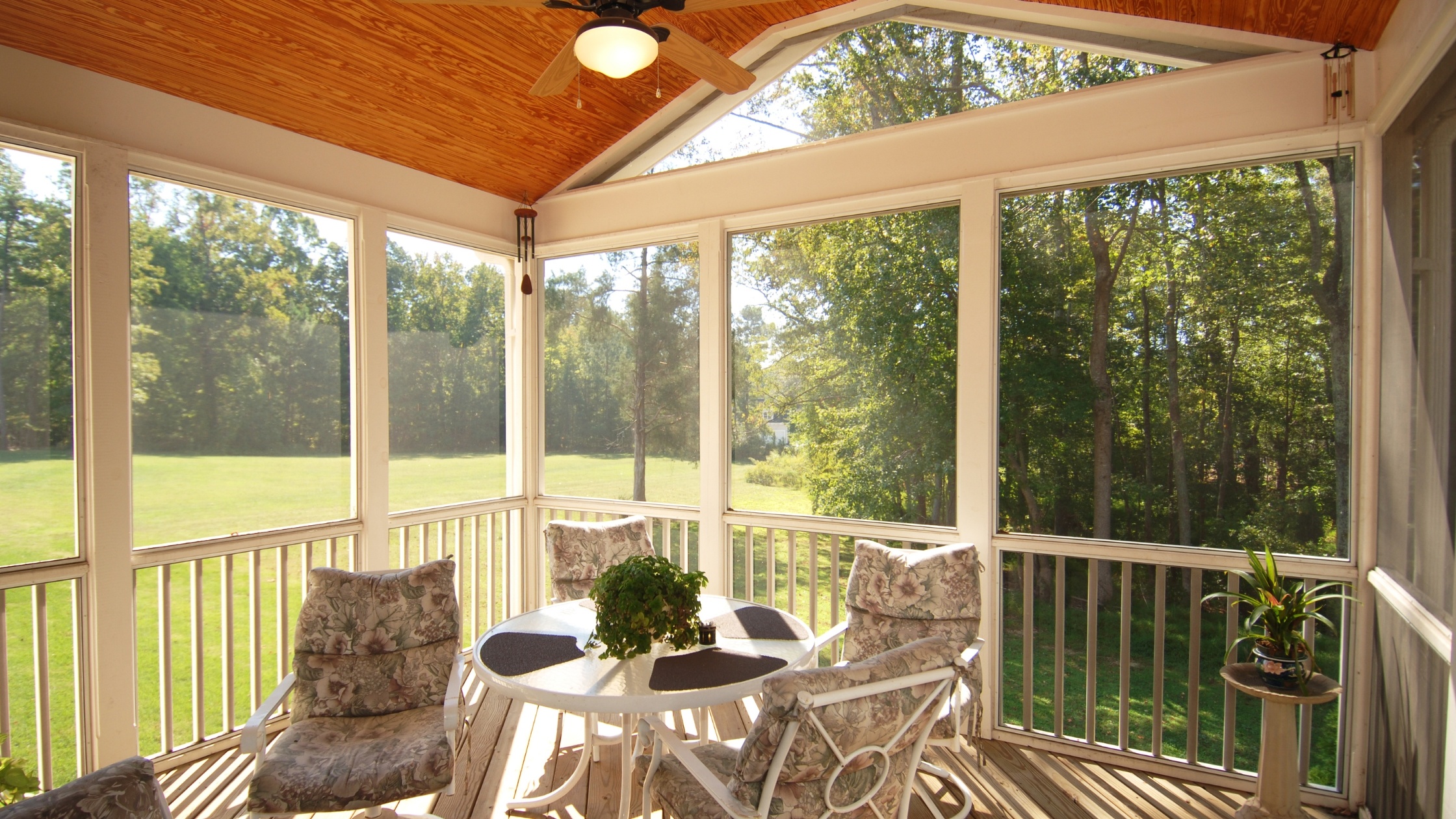 A beautiful screened-in back deck on a sunny day with lush green trees in the background.