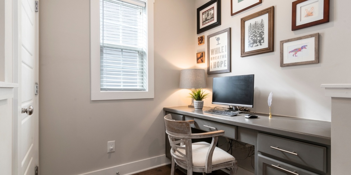 A small home office with a desktop monitor and keyboard on a desk with photos hanging on the wall behind.