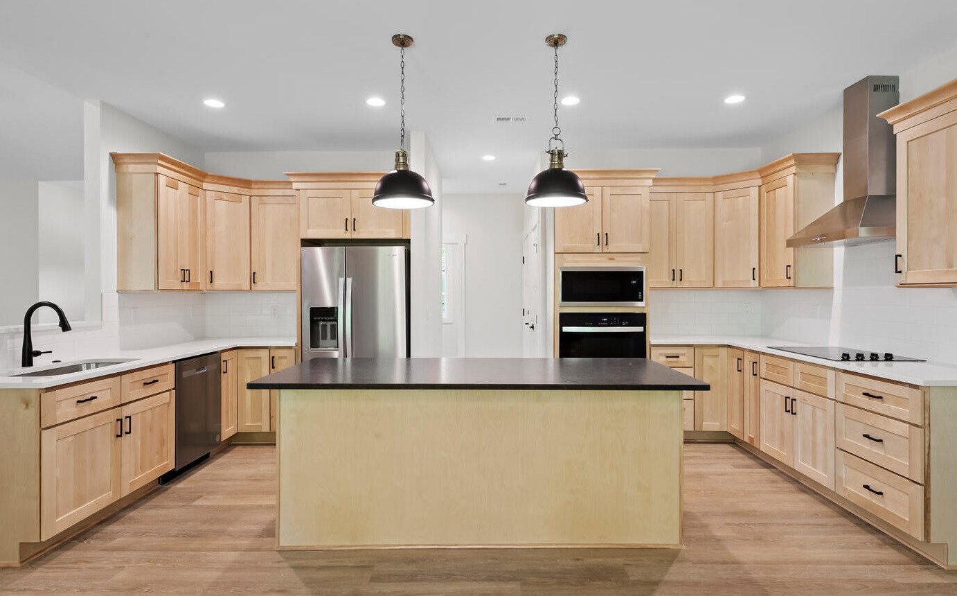 A kitchen in a home with white walls and clean wooden cabinets.