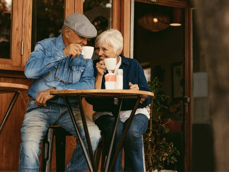 A couple of older folk have found their reason to retire and now enjoy sipping on coffee on a patio at a cafe.