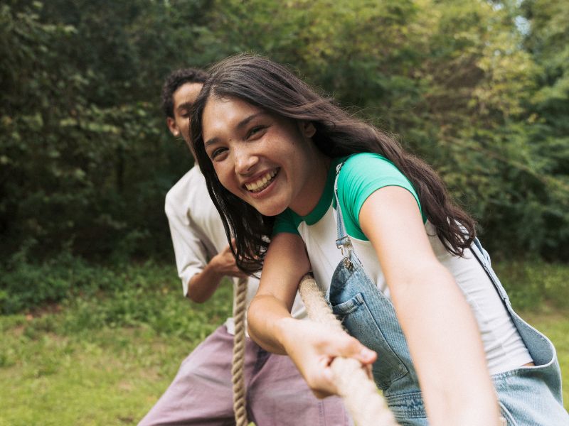 Two campers are pulling a rope in a game of tug-of-war outdoors.